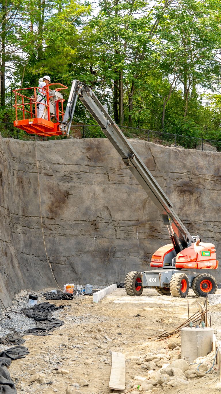 workers on crane spraying stone wall